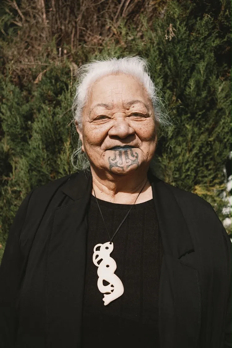 Portrait of Raiha Gray, a kuia with moko kauae and white hair, wearing a bone pendant.