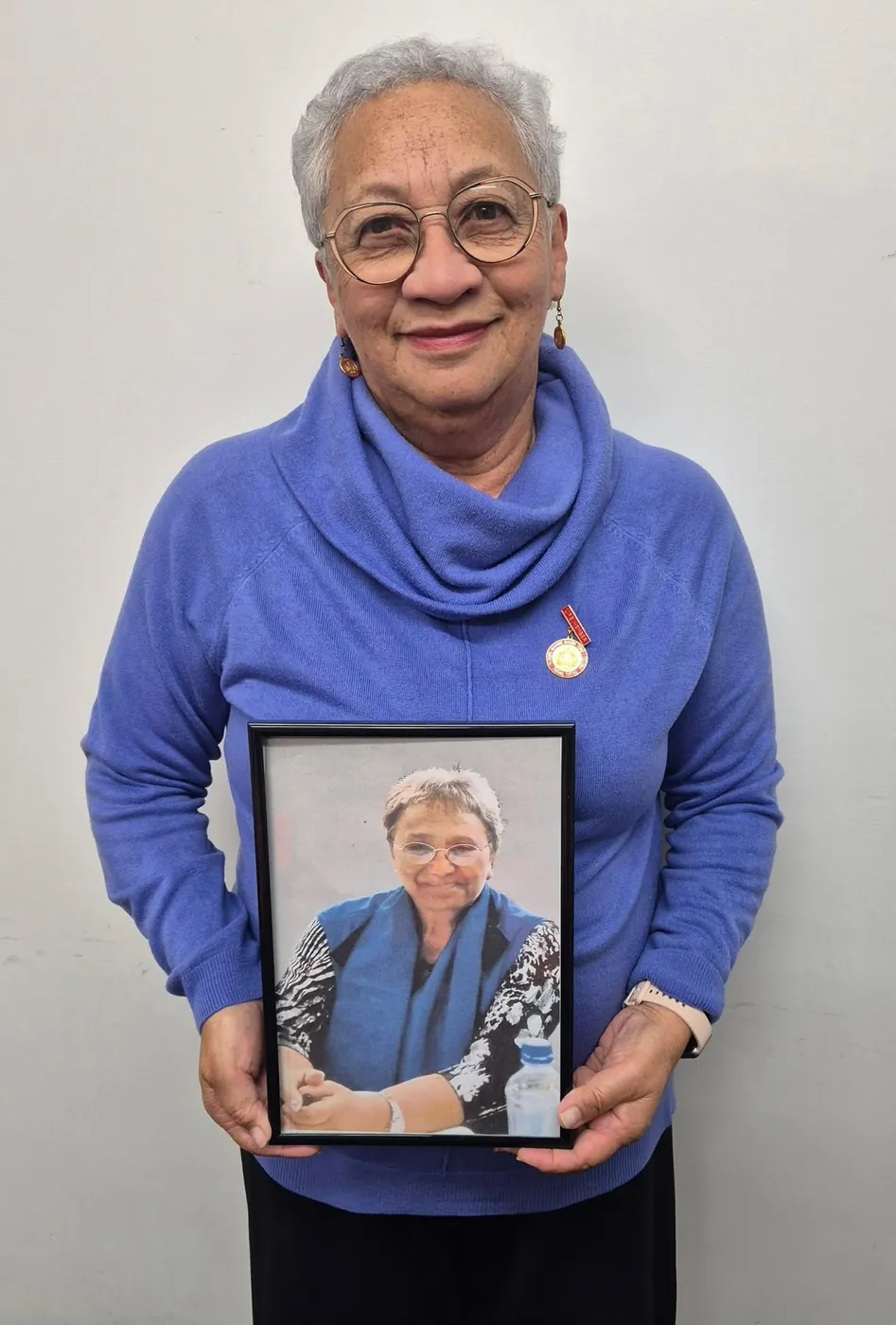 Woman in a blue jumper holding a framed portrait of a woman in a blue vest.