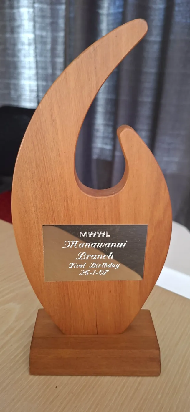 Close-up of the carved wooden one-year trophy with its plaque, on a wooden base.