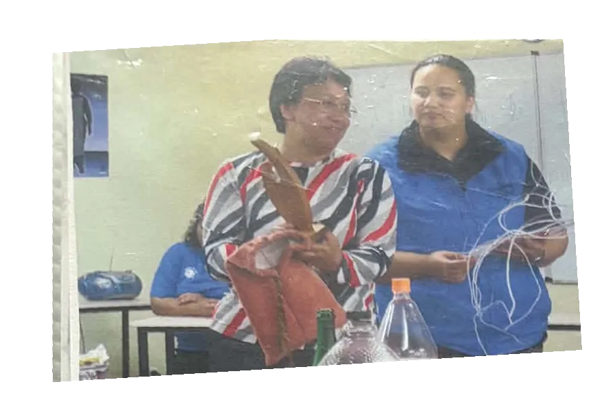 Two women holding up the wooden trophy and a woven piece in a meeting room.