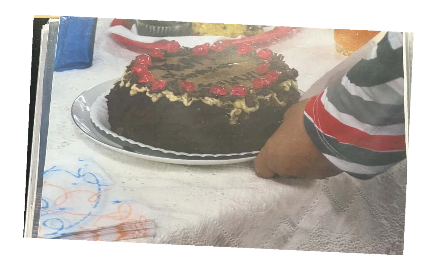A hand cutting into a chocolate cake topped with red berries.
