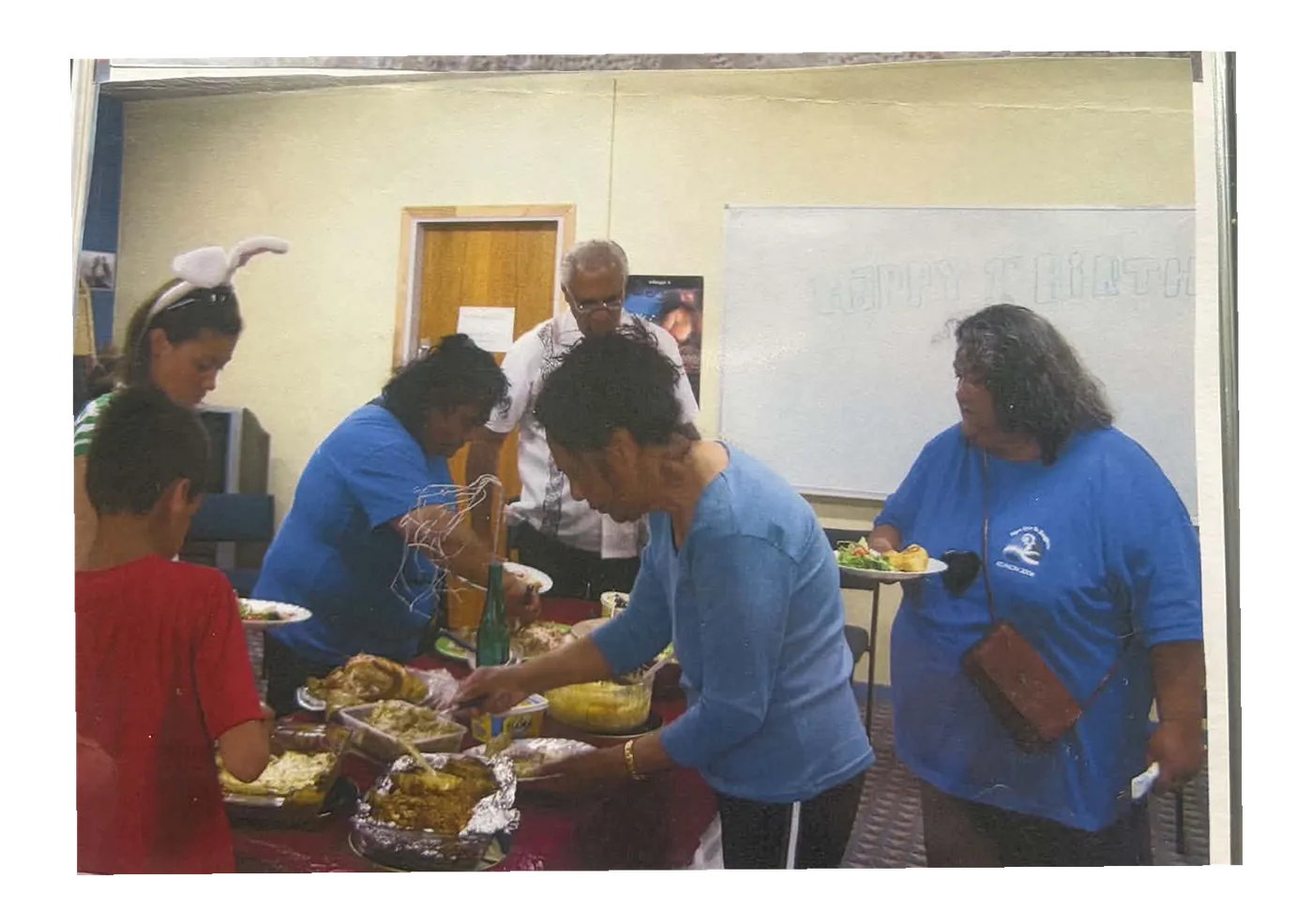 People filling their plates at a buffet table in a community hall.