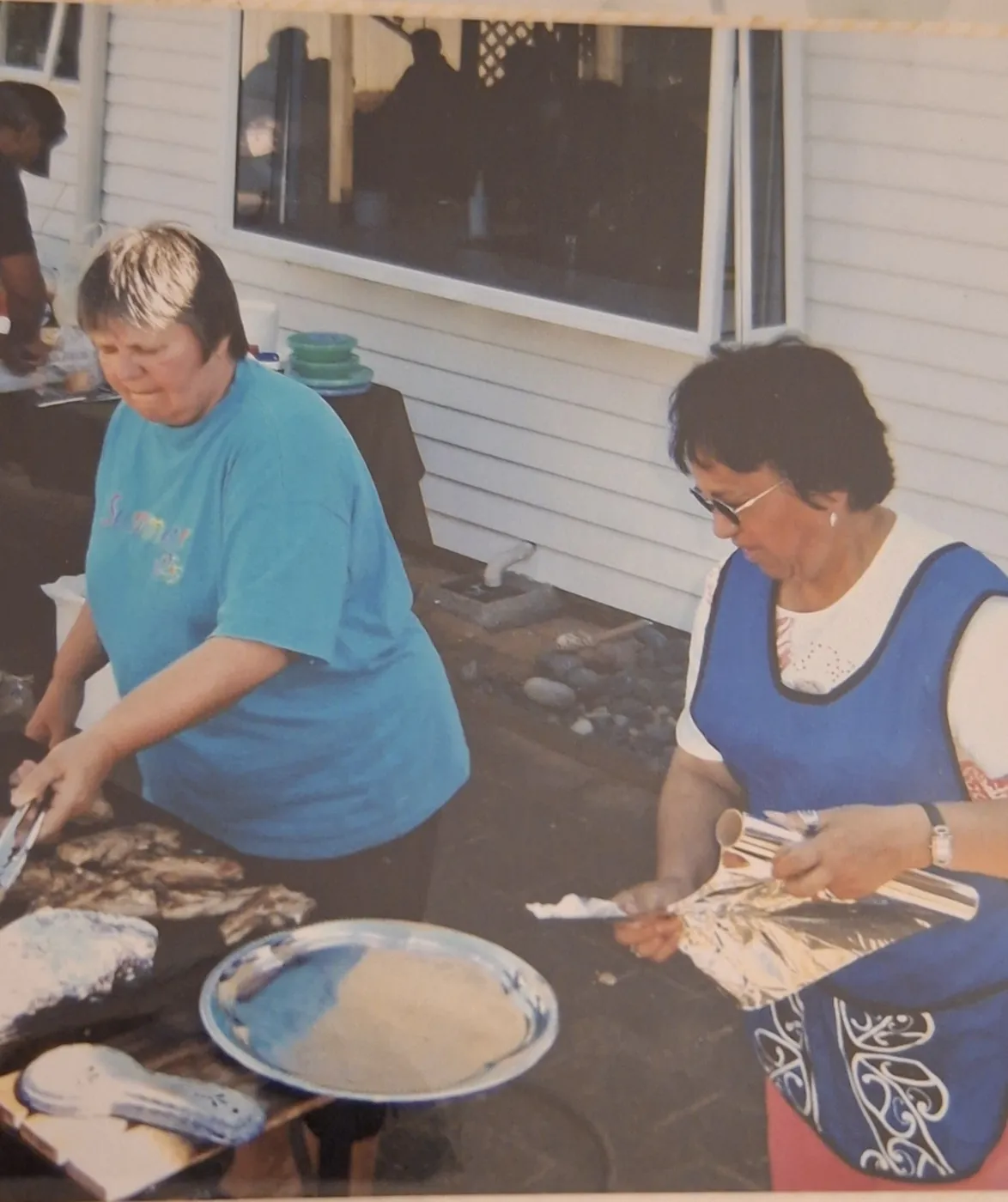 Two women serving food from platters at a kitchen bench.