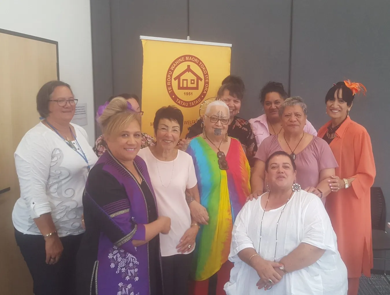 Group of smiling women in colourful clothes gathered in front of a yellow League banner.