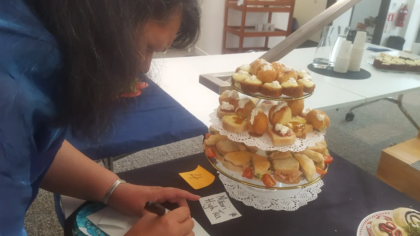 Woman writing a label beside a tiered stand of small filled bread rolls.