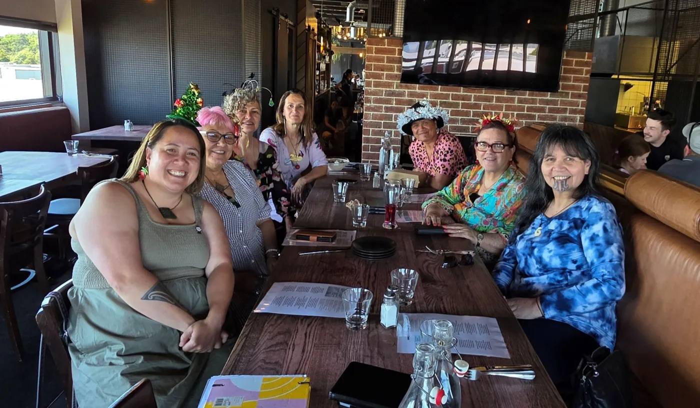 Seven women seated along a long restaurant table, smiling at the camera.