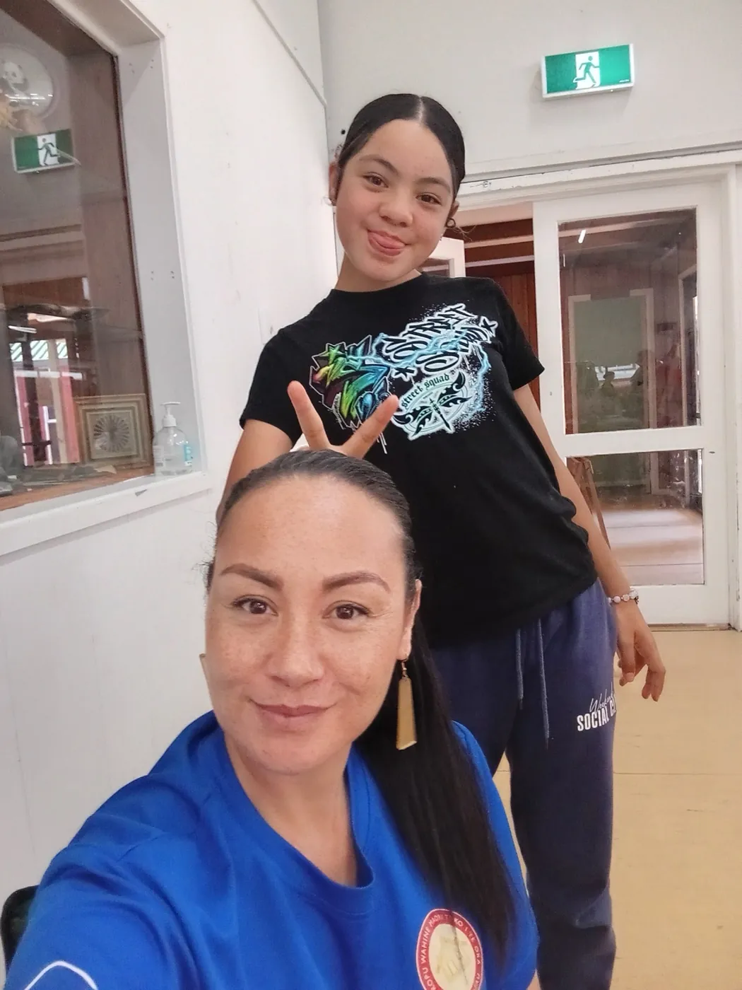 Woman in a blue top taking a selfie, with a young woman standing behind her.