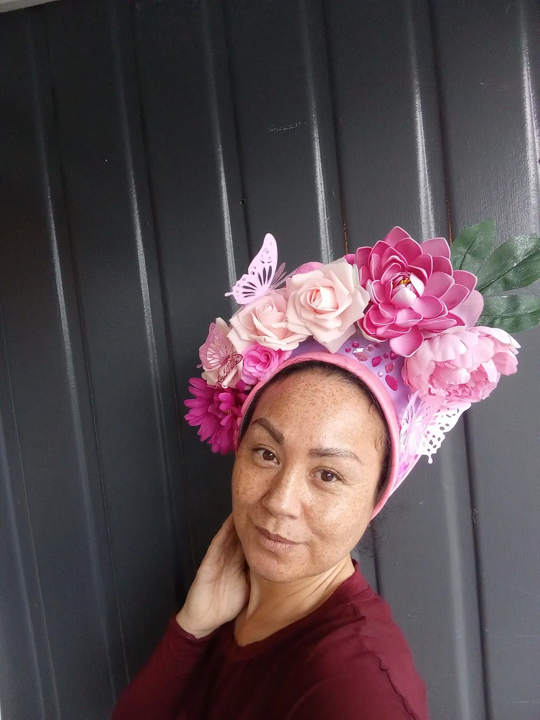 Woman wearing a pink floral fascinator made of paper roses and butterflies.