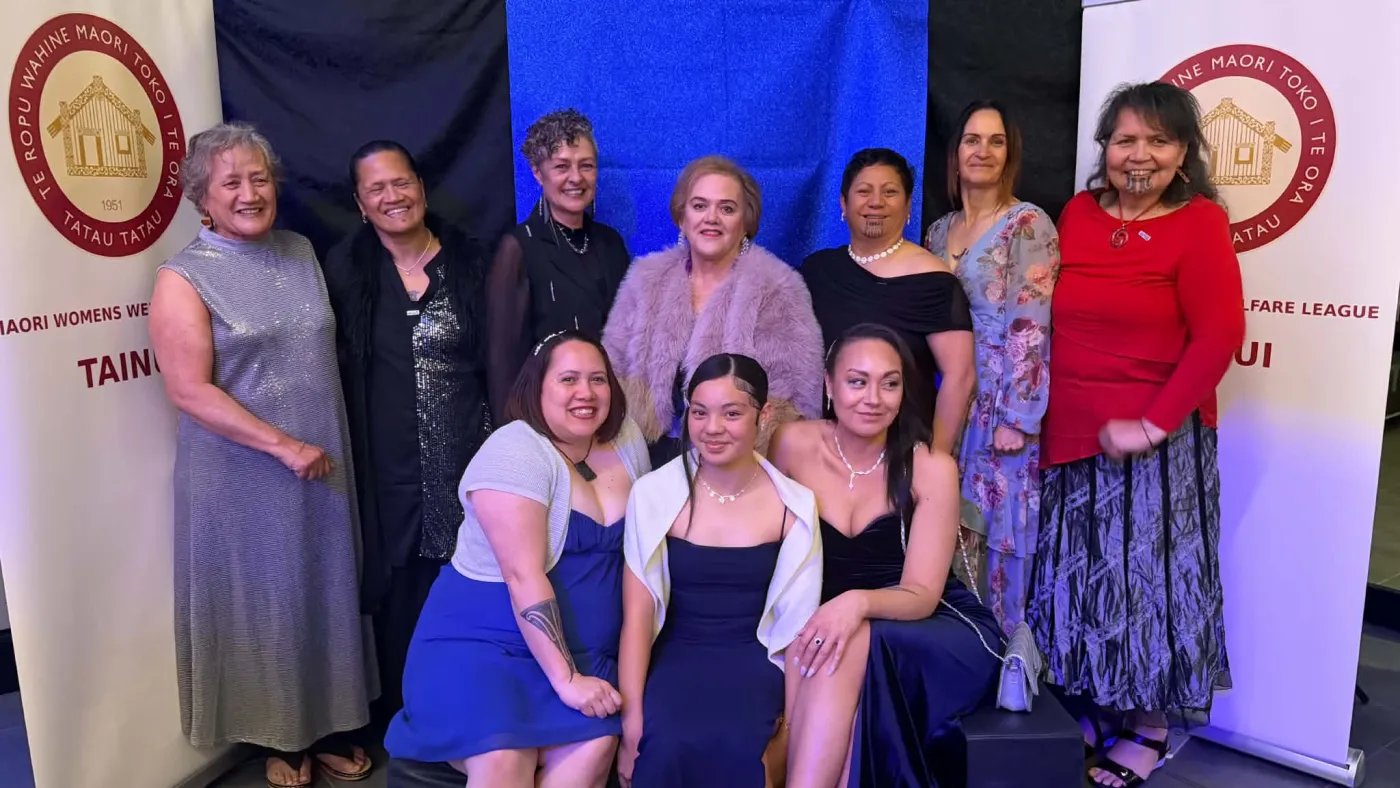 Ten Manawanui Peka members in formal dress, seven standing and three seated in front, between two Tainui Maori Women's Welfare League banners.